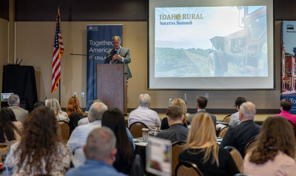 A man speaks at a podium in front of a large audience at a rural success summit