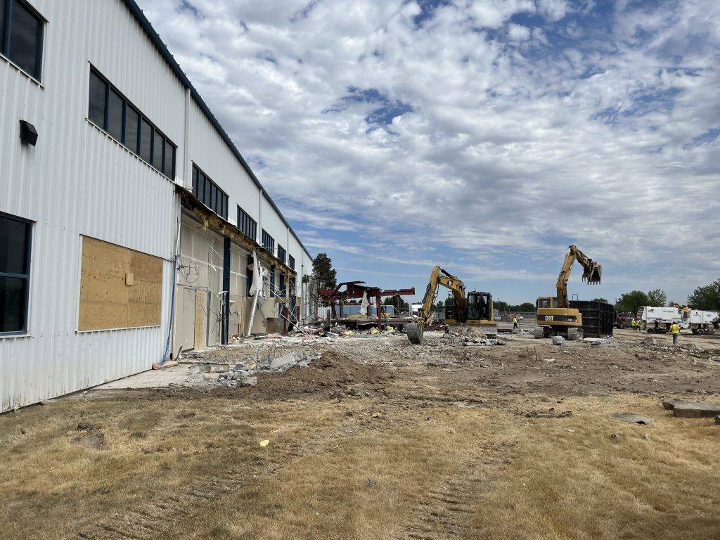 Demolition site of a partially collapsed white warehouse with heavy machinery and debris