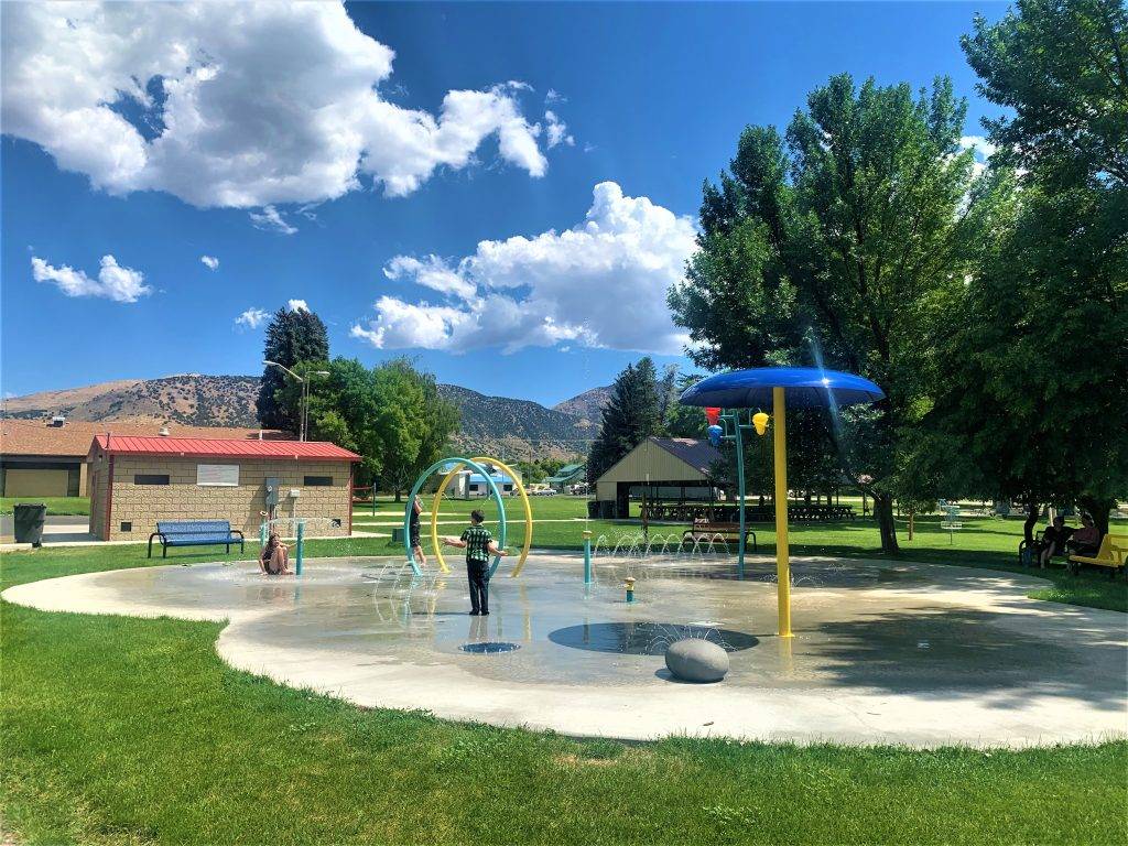A child plays in a splash pad with colorful equipment and a large umbrella in a park