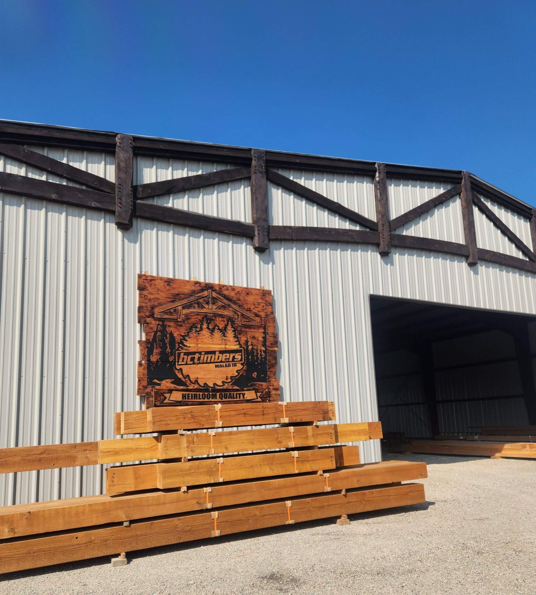 A large metal building with a sign for 'Octimbers' and stacked wooden beams outside