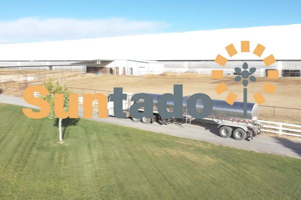 A tanker truck is parked on a road next to a large white building with a solar panel array