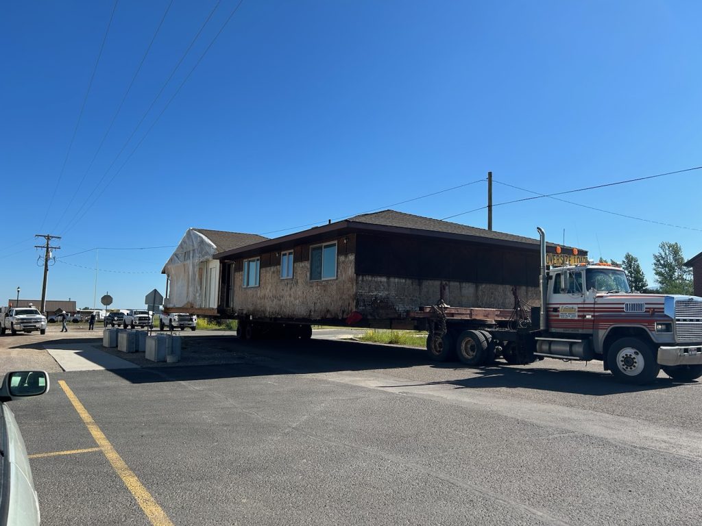 A large truck transports a prefabricated house on a trailer down a road