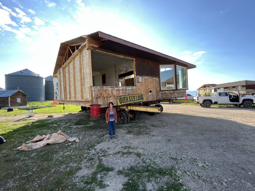 A partially constructed house is being transported on a flatbed truck with a sign indicating 'OVERSIZE LOAD'