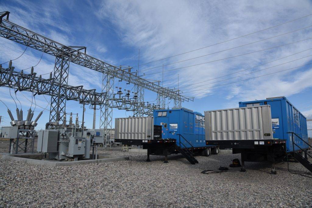 Blue shipping containers and electrical substation equipment under a cloudy sky