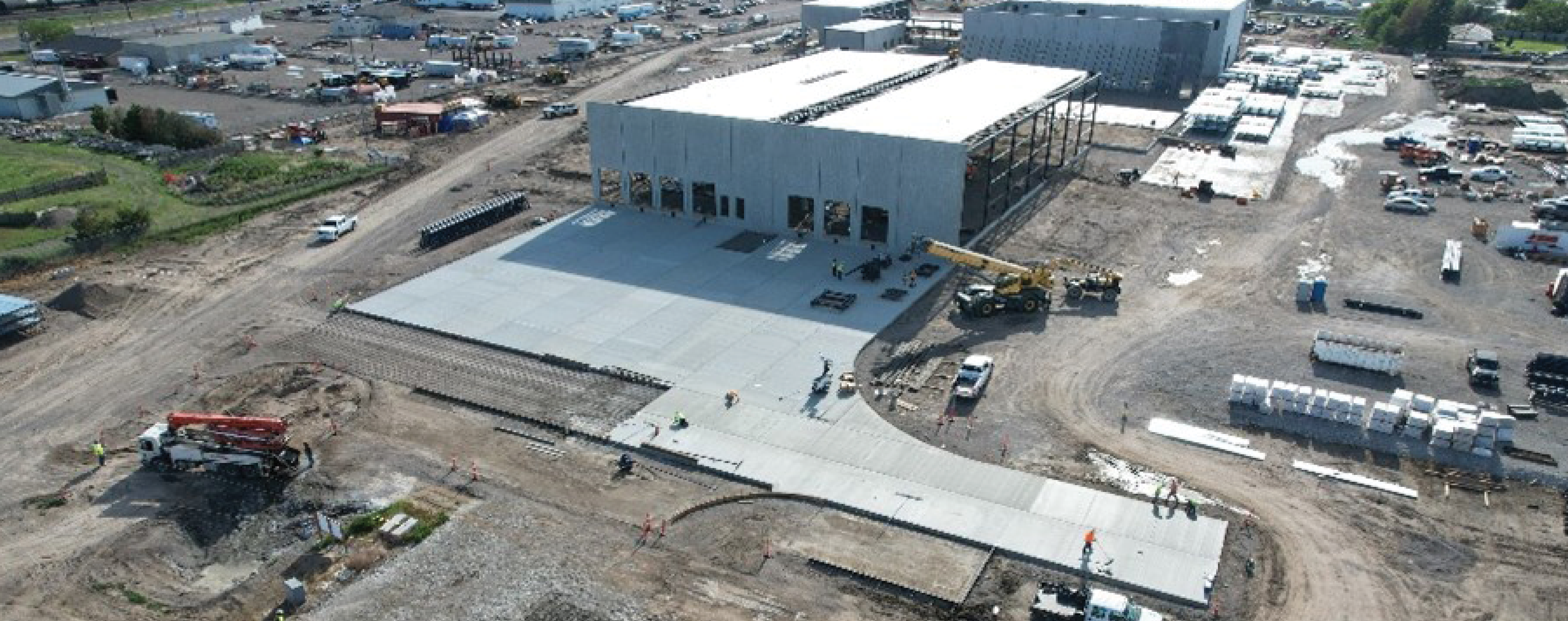 Aerial view of a large industrial construction site with multiple buildings, cranes, and vehicles