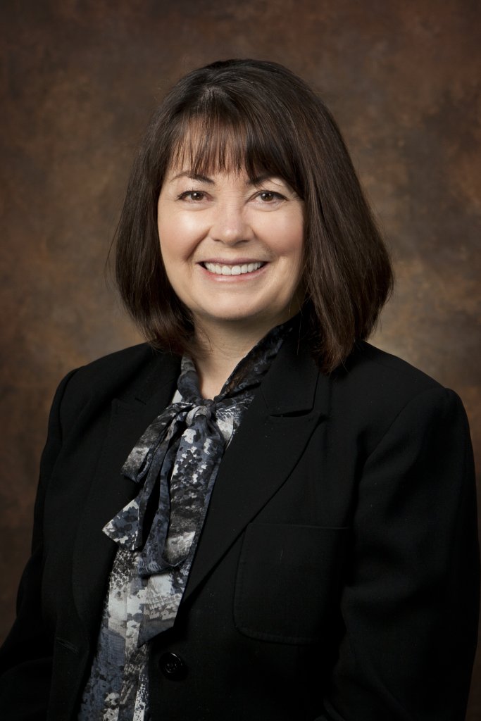 A smiling woman with shoulder-length dark hair wearing a black blazer and patterned blouse
