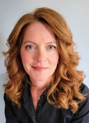 A woman with long, wavy red hair smiles warmly at the camera
