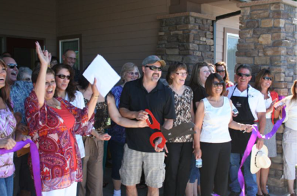 A diverse group of people celebrate a ribbon-cutting ceremony outdoors