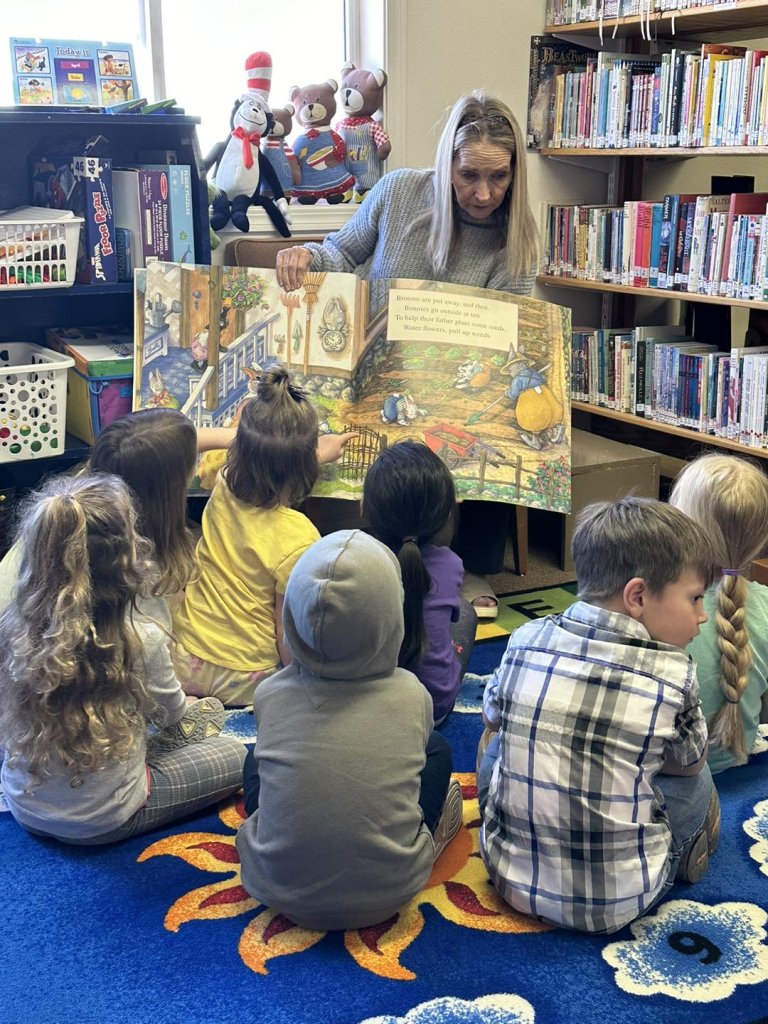 A librarian reads a colorful picture book to a group of attentive children on a vibrant rug