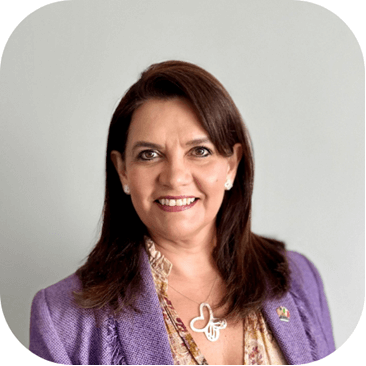 A smiling woman with long brown hair wearing a purple jacket and a butterfly necklace