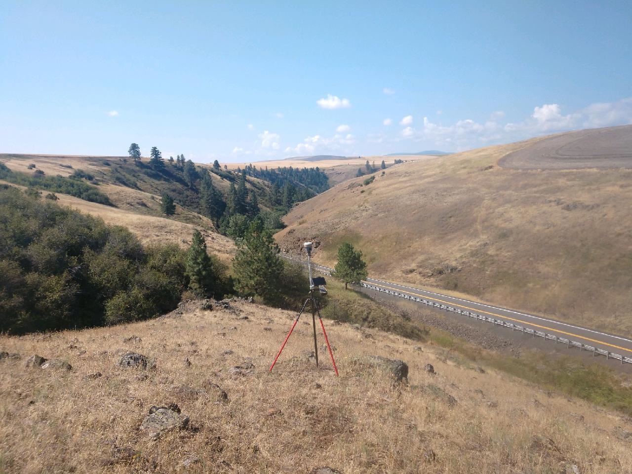 A camera mounted on a tripod captures a scenic view of rolling hills and a winding road