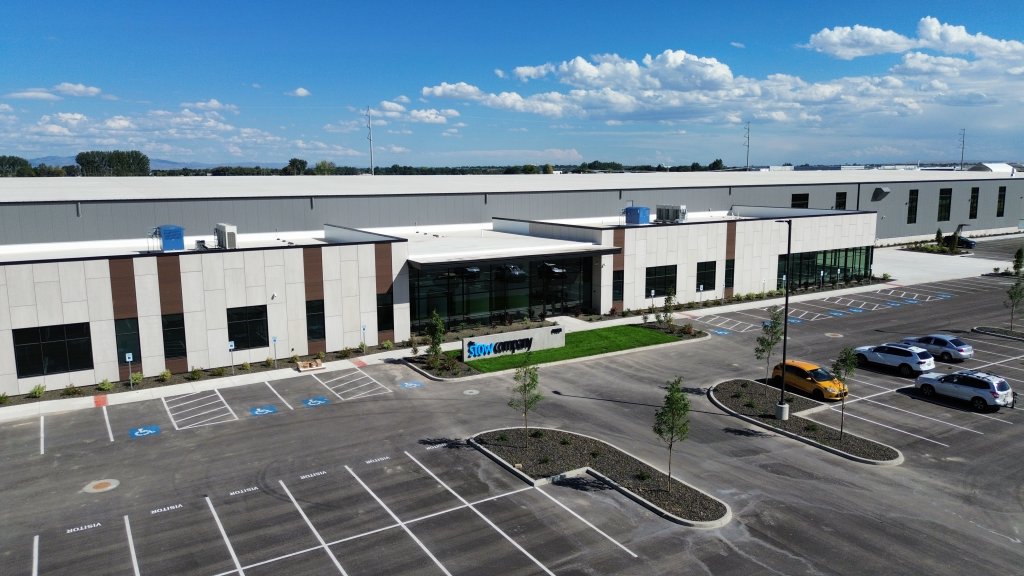 Aerial view of a modern industrial building with a large parking lot and several cars