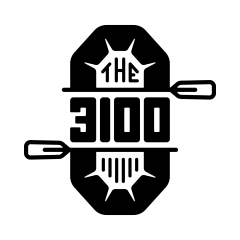 A black cat with a white chest and paws sits on a wooden floor