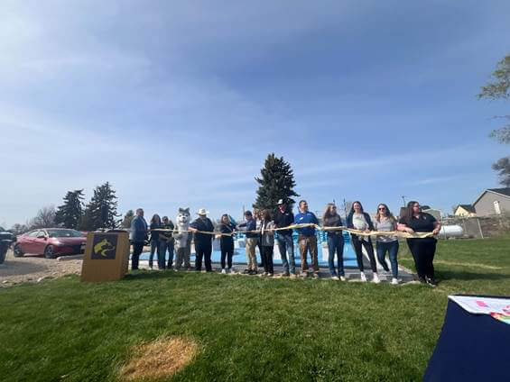 A group of people stand together outdoors, holding a ribbon for a ceremonial cutting