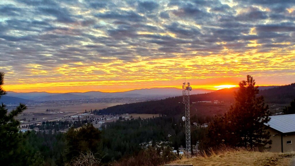 A breathtaking sunset paints the sky with vibrant hues of orange and yellow, casting a warm glow over the distant mountains and the sprawling city below
