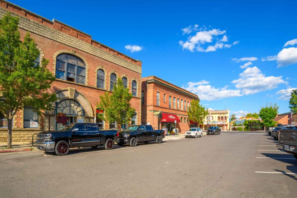 A picturesque small town street lined with historic brick buildings and modern vehicles parked along the curb