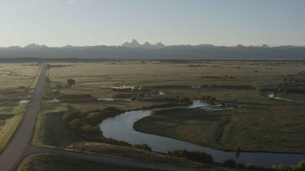 Aerial view of a vast, open landscape with a winding river, fields, and distant mountains under a clear sky